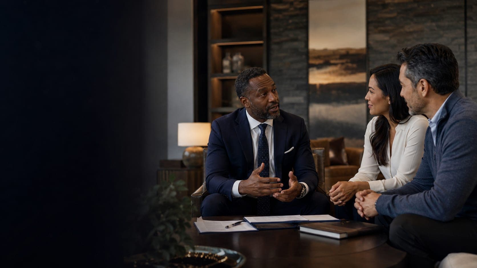 A financial advisor in conversation with a client couple in a warm, low-lit study